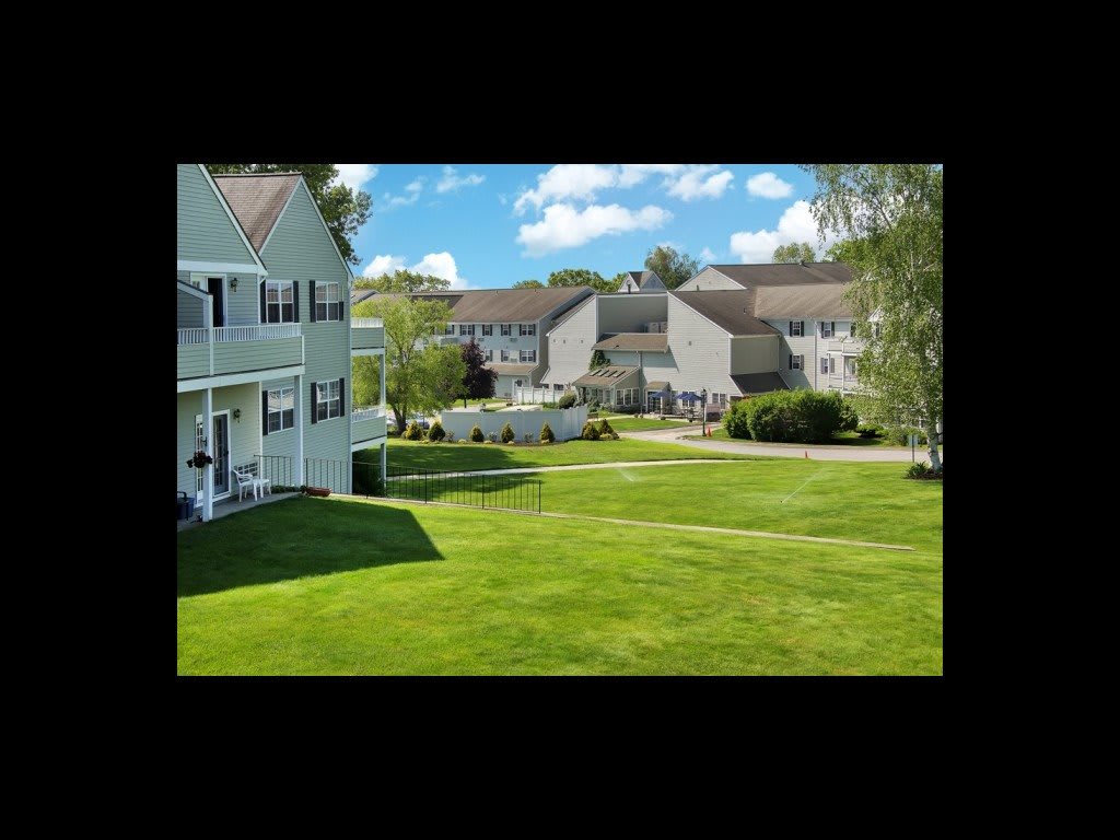 A view of apartment buildings surrounding a well-kept grassy courtyard under a partly cloudy sky.