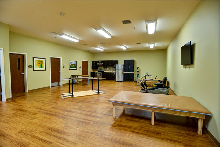 A spacious rehabilitation room equipped with exercise equipment and a therapy bed.