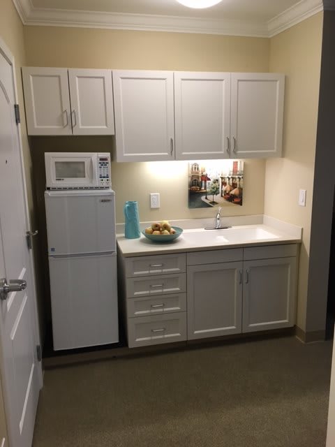 A compact apartment kitchen with white cabinets, a microwave, and a small fridge.