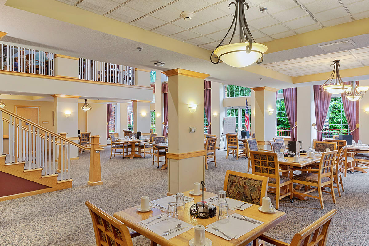 A spacious and elegantly decorated dining room with multiple tables and chairs, featuring a large chandelier.