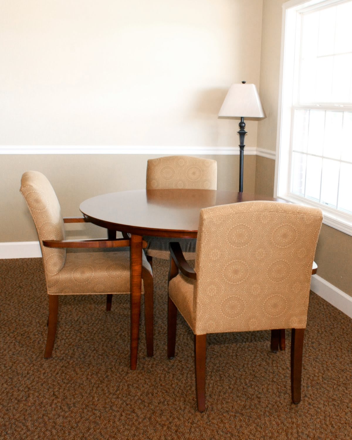 A cozy room with a round table and three chairs, accompanied by a standing lamp near a window.