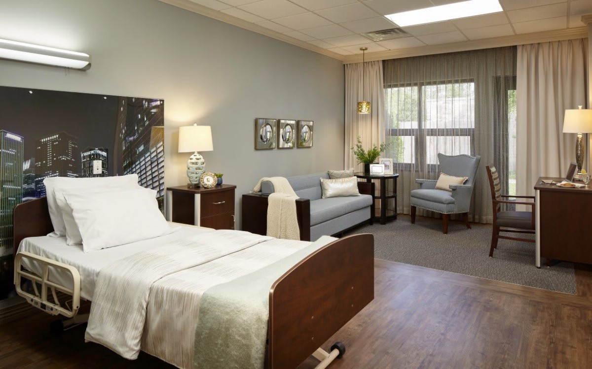 A modern and well-furnished hospital room with a patient bed, sofa, and seating area.