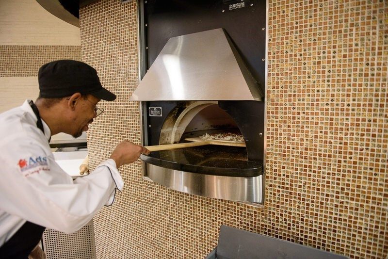 A chef places a pizza in a stone oven at a restaurant.