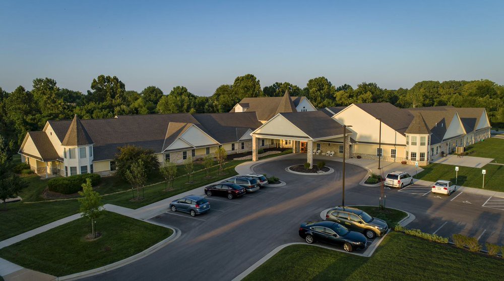 Aerial view of a building with a parking lot and cars, surrounded by trees at sunset.