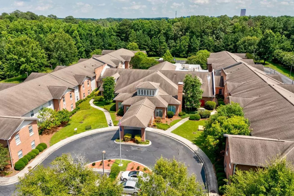 Aerial view of residential buildings surrounded by lush greenery and a circular driveway.
