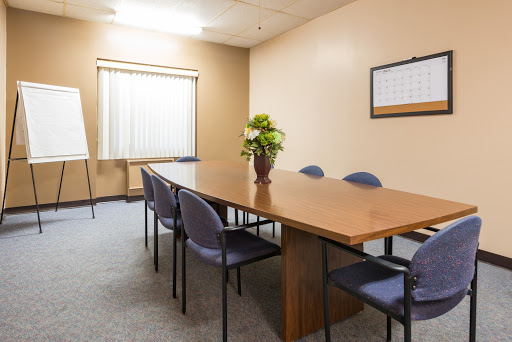 A neatly arranged conference room equipped with a wooden table and comfortable chairs, ready for discussions.