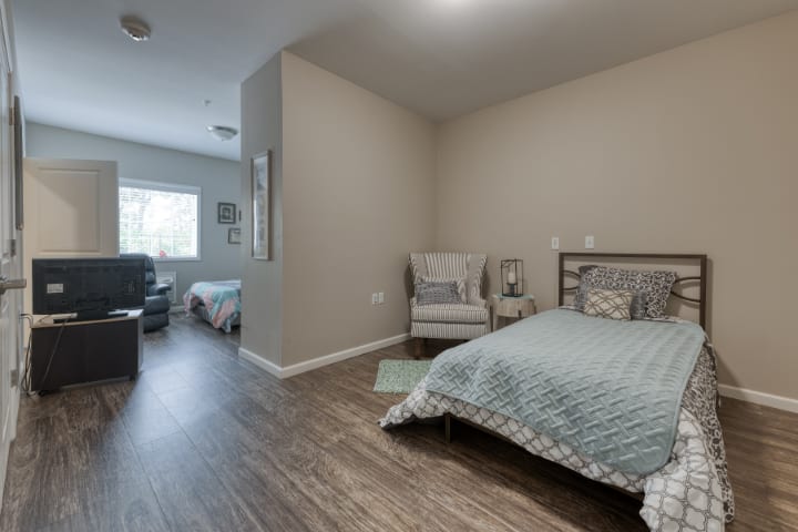A modern bedroom with wooden flooring, featuring a cozy bed and a comfortable chair near the window.