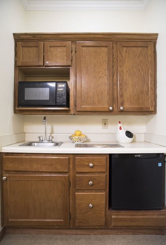 A compact kitchen setup with wooden cabinets, a microwave, a sink, and a mini fridge.