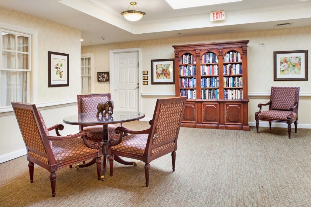 A cozy library interior with a round table, chairs, and a bookshelf filled with books.