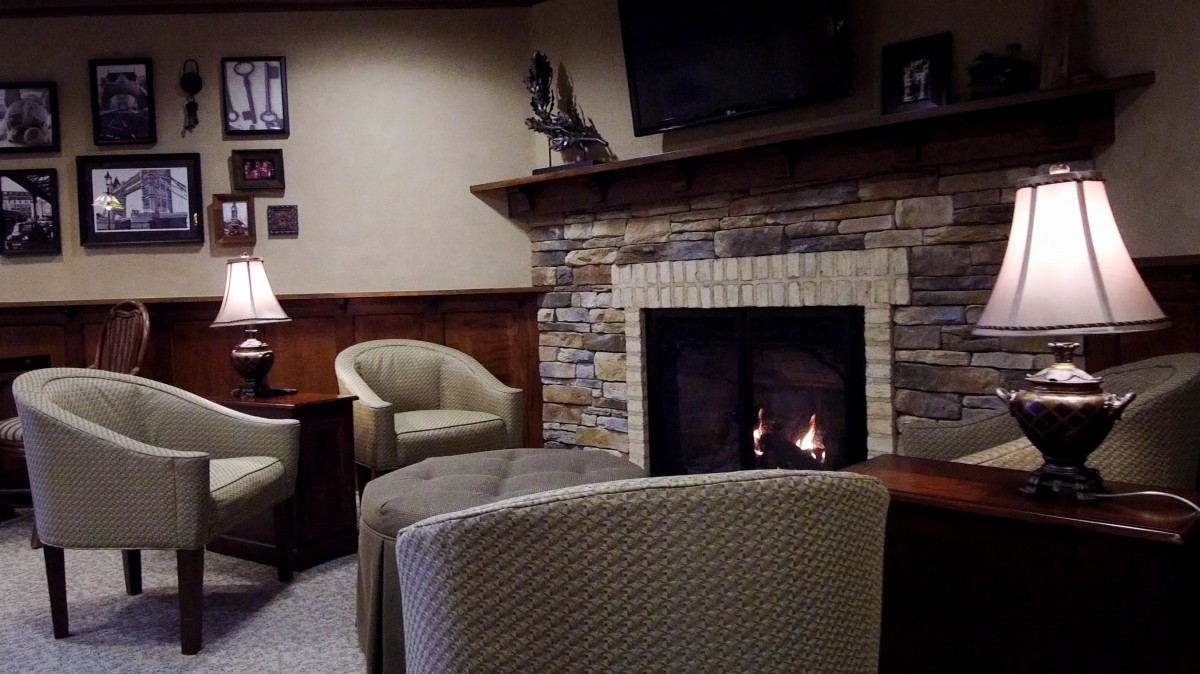 A cozy living room featuring a stone fireplace, comfortable armchairs, and a TV mounted above.