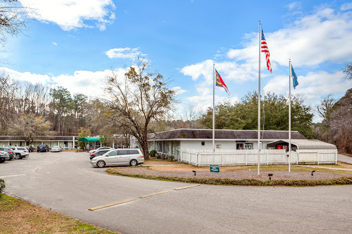 A view of a building with multiple flags in front, set against a backdrop of blue skies and trees.
