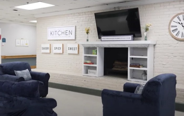 A cozy living area featuring a wall-mounted TV, comfortable seating, and decorative shelves in a kitchen-themed space.