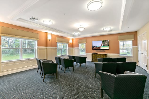 A conference room with multiple chairs facing a television, featuring large windows and bright lighting.