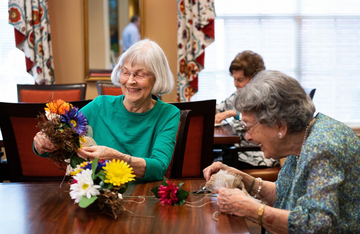 A group of senior women happily engaging in a crafting activity, arranging flowers together indoors.