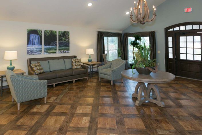 A stylish living room with wooden flooring, featuring a sofa set, armchairs, a coffee table, and a chandelier.