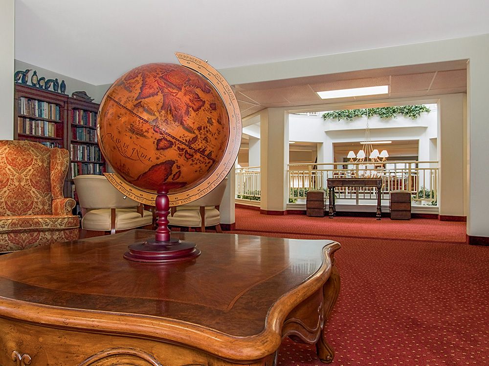 An elegant library interior featuring a globe on a wooden table, surrounded by bookshelves and comfortable seating.