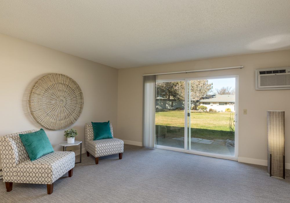 A bright and airy living room featuring two chairs and a large sliding glass door leading to an outdoor space.