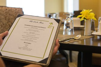 A person holding a menu in a restaurant with a table set elegantly with glasses, cutlery, and flowers.