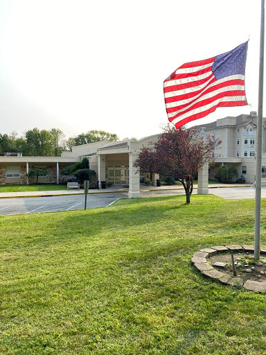 A view of a building with an American flag waving in the foreground, surrounded by a well-maintained lawn.