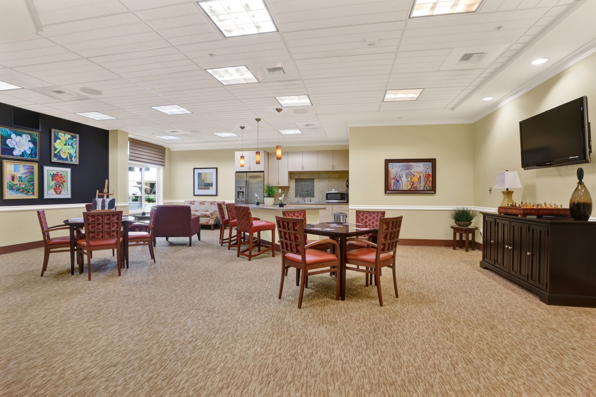 A spacious dining area with multiple tables and chairs arranged on a carpeted floor, well-lit by ceiling lights.