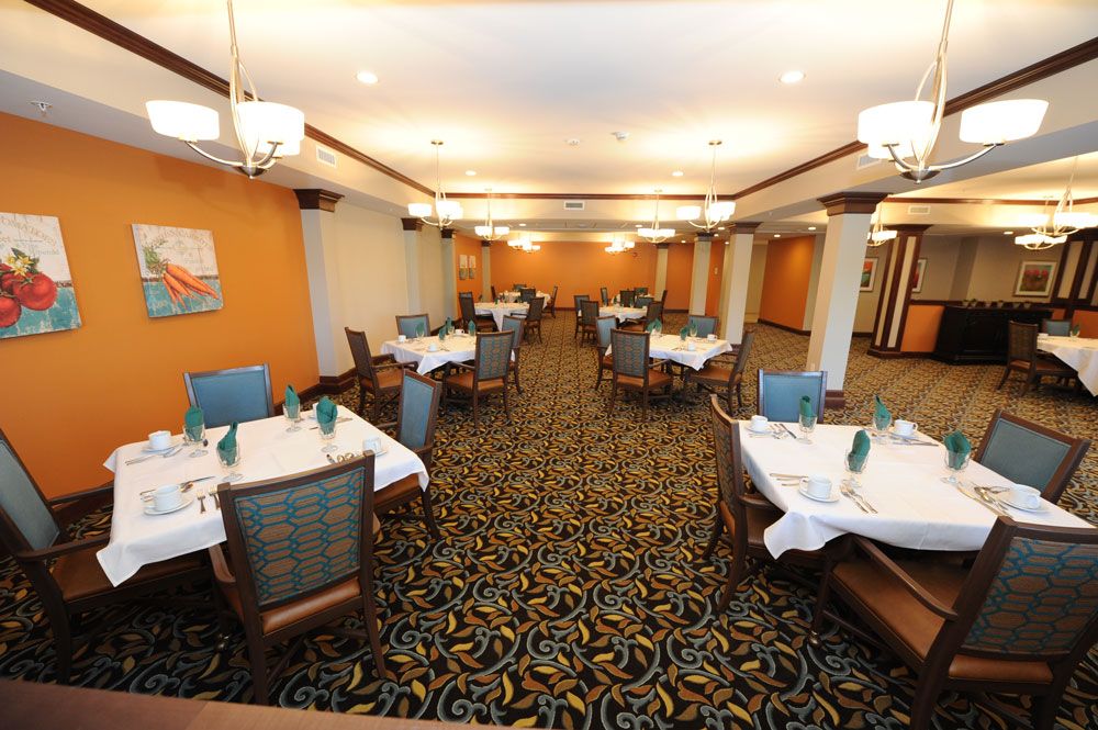 An elegant dining room with neatly arranged tables and chairs, featuring a patterned carpet and warm lighting.