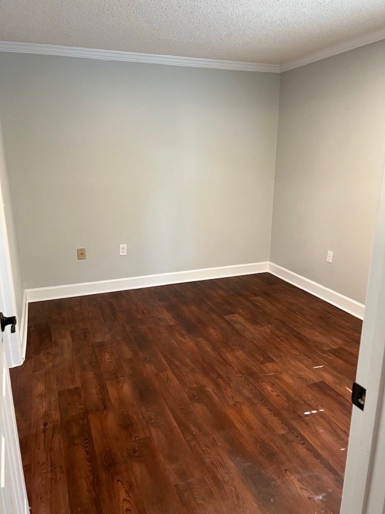 An empty room with wooden flooring and plain white walls.