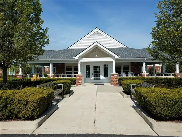 A symmetrical building with a central entrance, surrounded by neatly trimmed hedges and trees along a paved walkway.