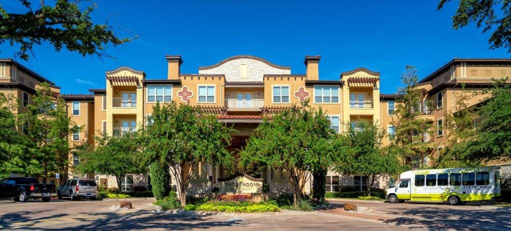 A residential building with a prominent entrance and surrounding greenery under a clear blue sky.