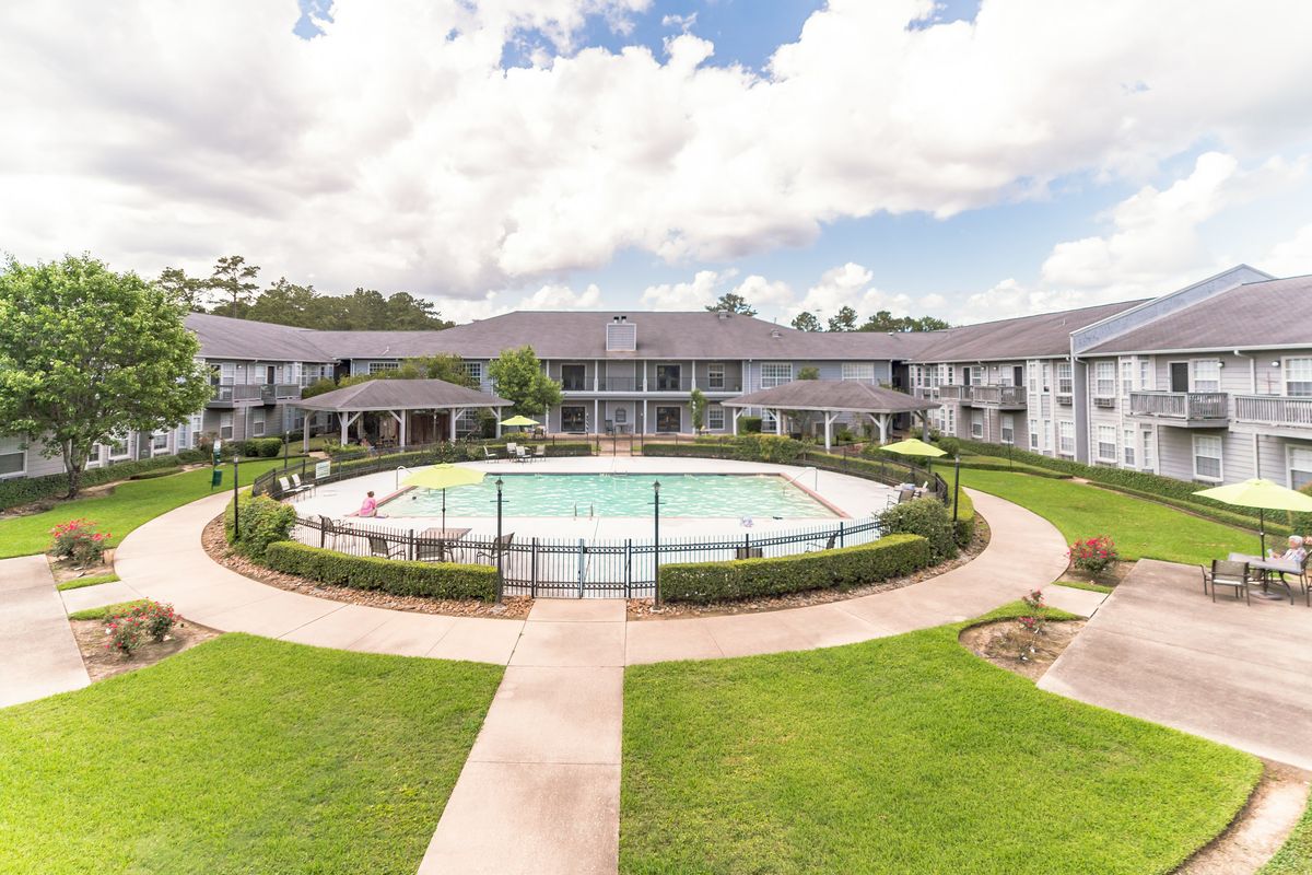 A scenic view of an apartment complex with a central swimming pool surrounded by landscaped greenery and pathways.