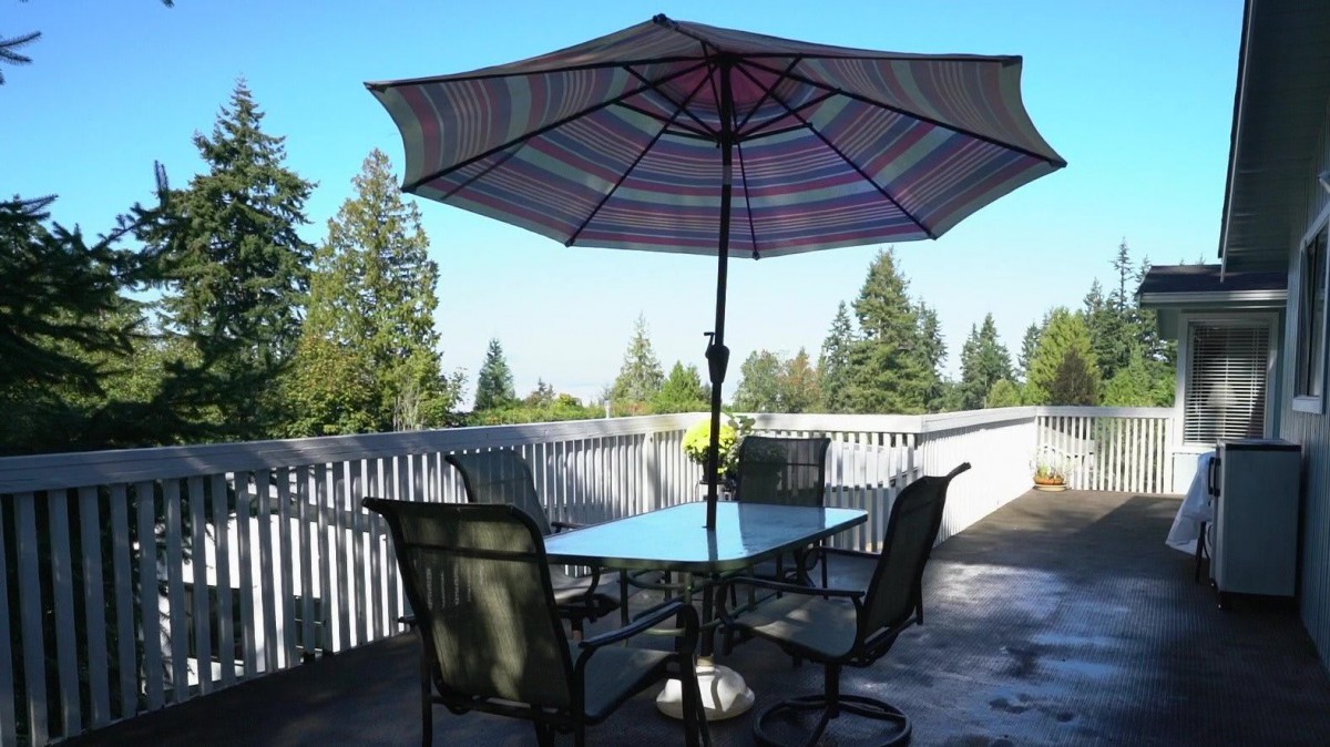 A patio set with an umbrella on a deck overlooking trees.