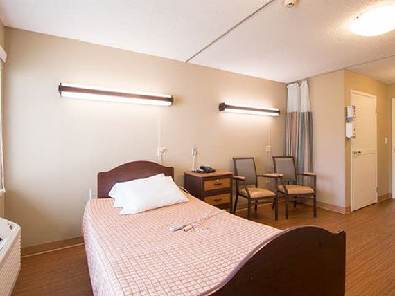 A simple hospital room with a single bed and seating area.