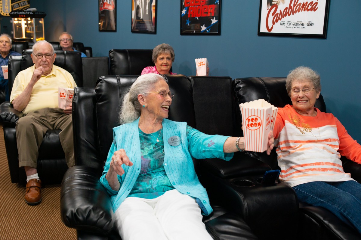 A group of seniors enjoying a movie in a comfortable cinema setting with recliner seats and popcorn.