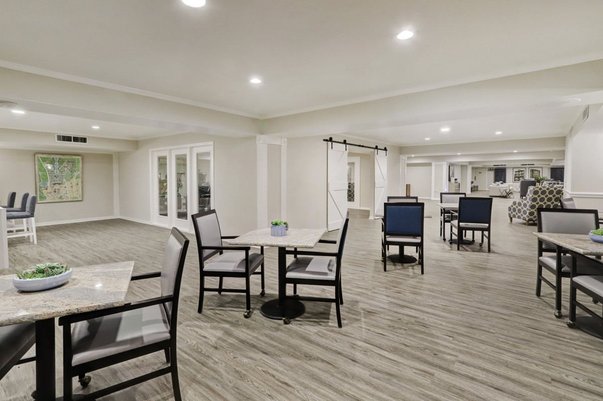 A spacious and modern dining area with tables and chairs, featuring a hardwood floor and bright lighting.