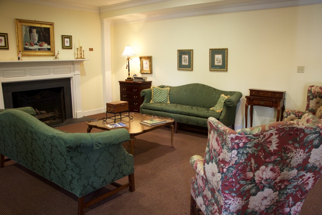 A cozy living room with traditional furniture and decor, featuring a green sofa, floral armchair, and a coffee table set on a carpet.