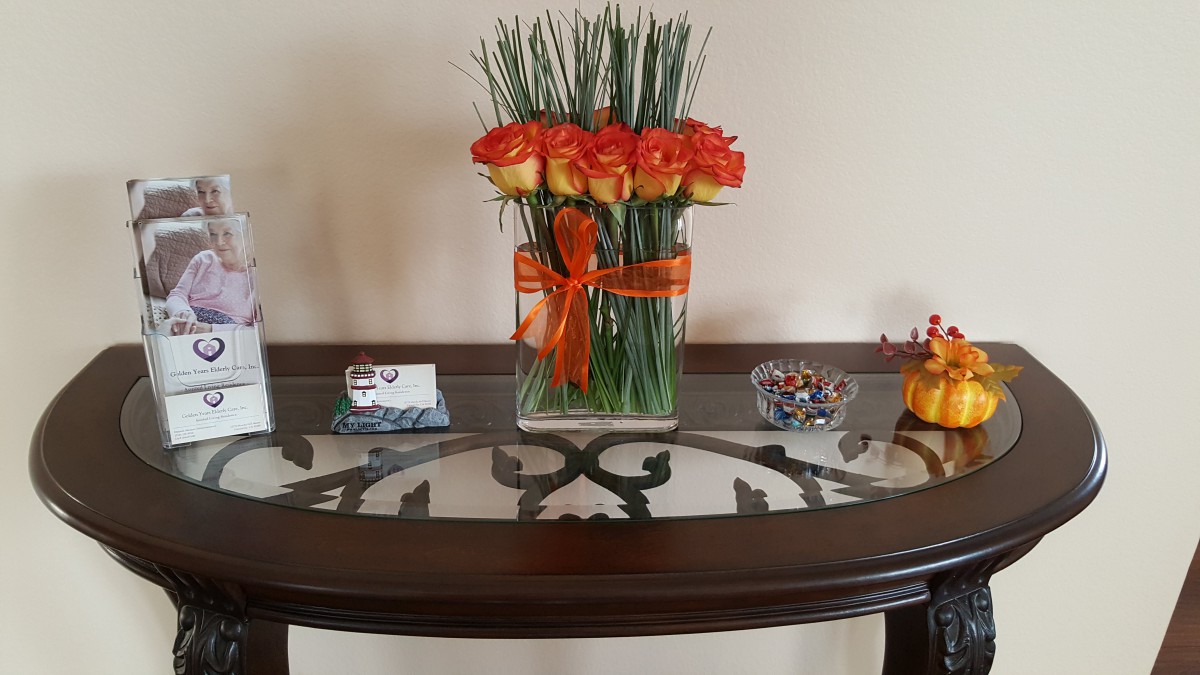 A decorative arrangement of orange roses in a vase with a matching ribbon, displayed on a glass-top table.