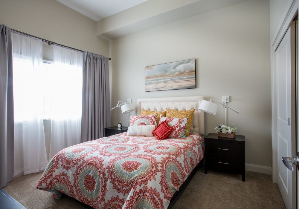 A cozy bedroom featuring a bed with patterned bedding and decorative pillows, accompanied by bedside tables and an artwork piece on the wall.