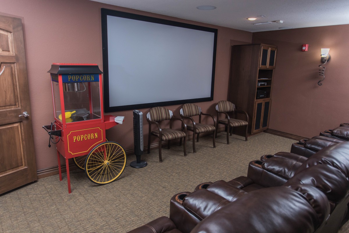 A cozy home theater setup featuring a large projector screen, comfortable leather couches, additional seating chairs, and a popcorn machine for an authentic movie experience.