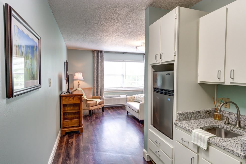 A modern apartment interior featuring a small kitchen area leading into a bright living room with hardwood flooring.