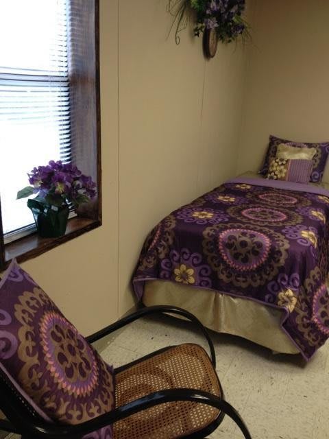 A cozy bedroom with purple-themed bedding and a chair by the window.
