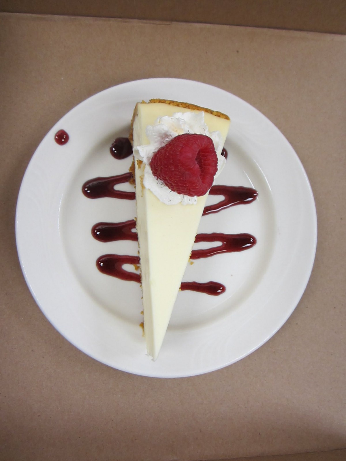 A slice of cheesecake topped with a strawberry and drizzled with berry sauce on a white plate.