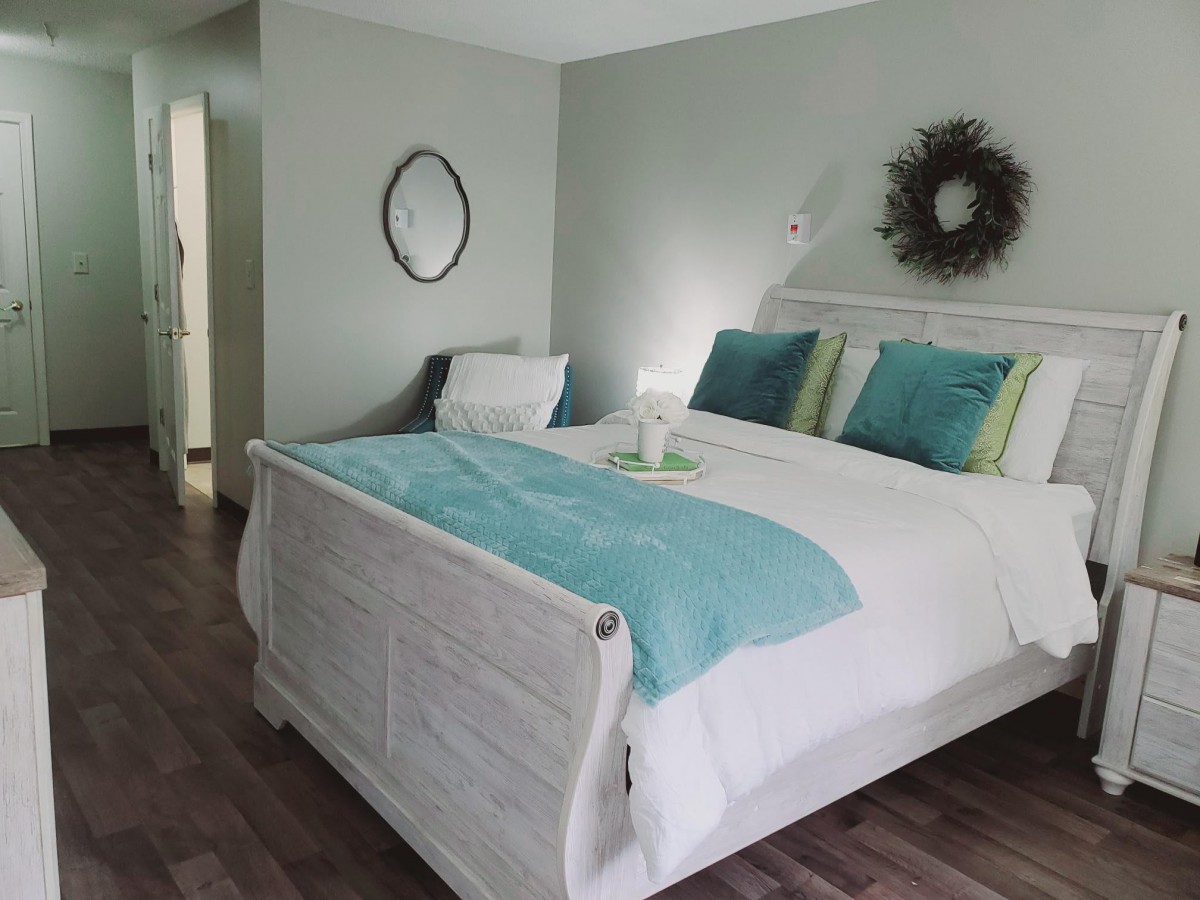 A modern bedroom with stylish decor, featuring a neatly made bed with teal and white bedding and pillows.
