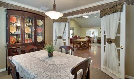 A cozy dining room with a lace-covered table and a china cabinet displaying decorative plates.