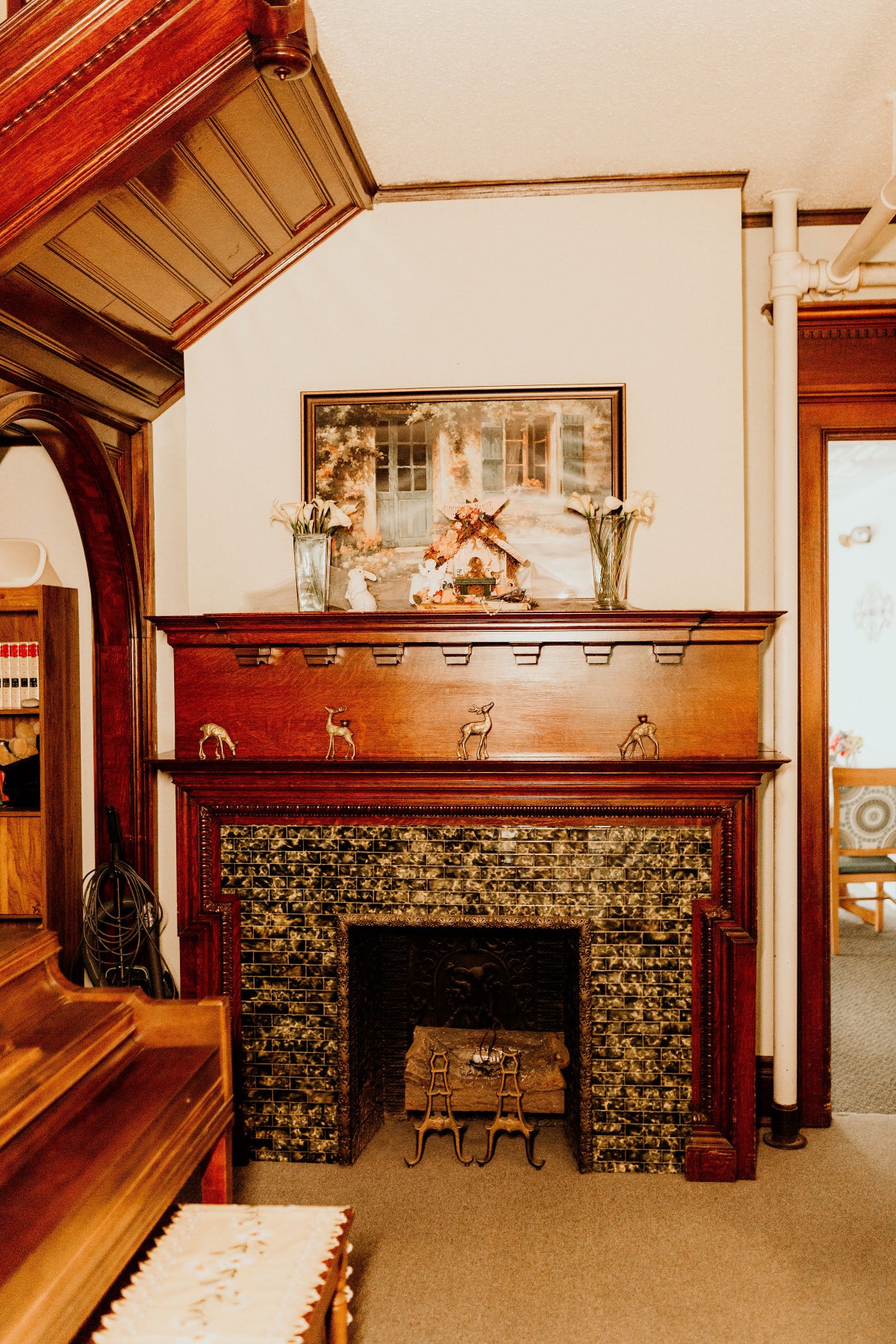 A cozy vintage room with an ornate wooden fireplace and artwork above the mantel.