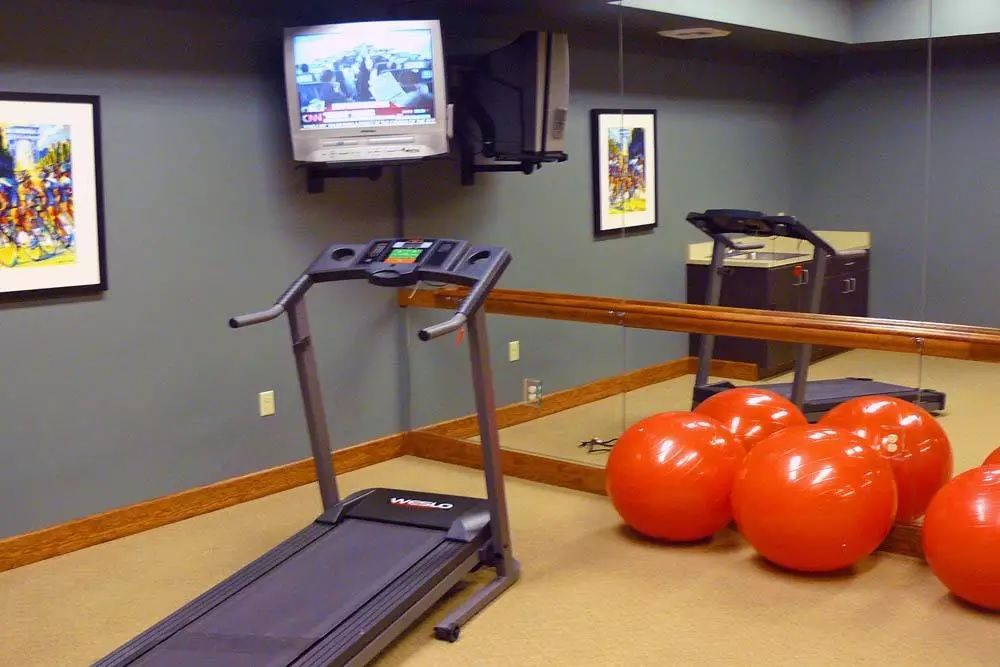 A small gym with a treadmill, exercise balls, and a wall-mounted television.