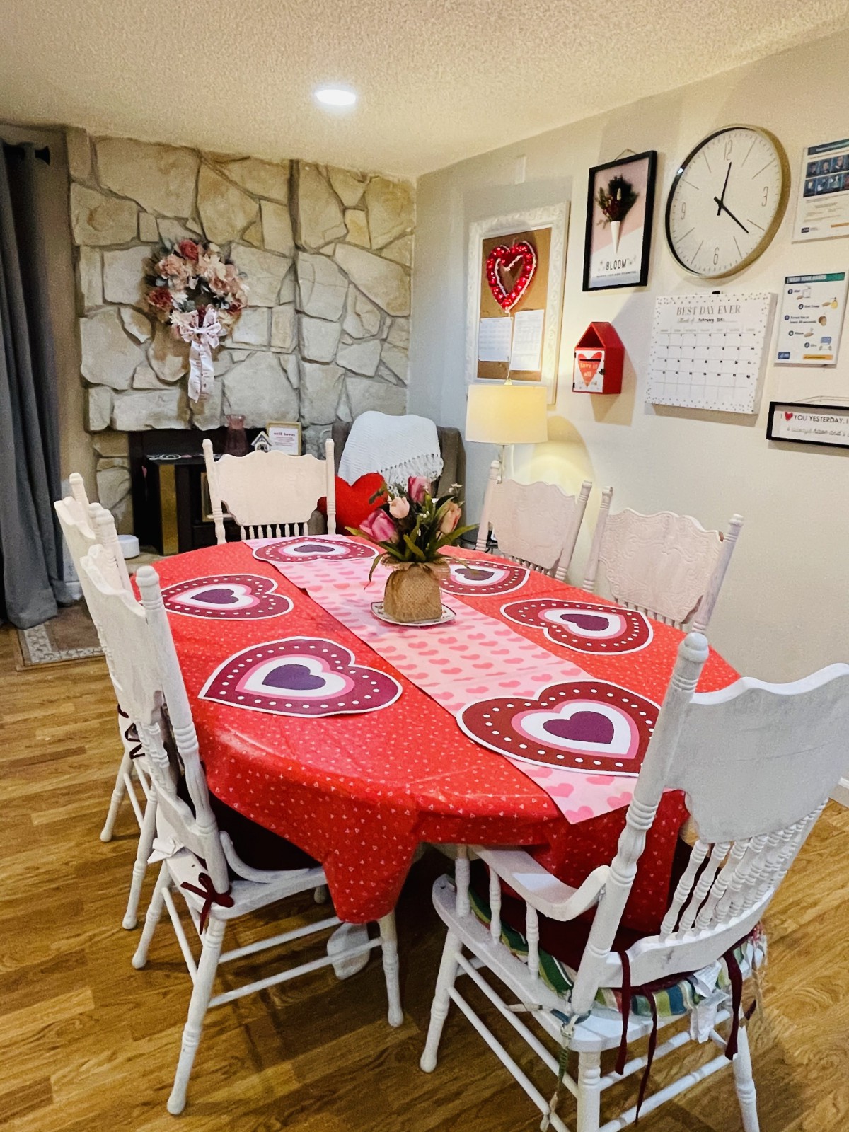 A dining room adorned with Valentine's Day decorations, featuring a red tablecloth with heart patterns, surrounded by white chairs and a floral centerpiece.