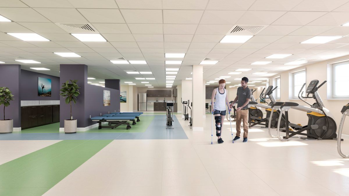 Two people walking in a rehabilitation center equipped with exercise machines.