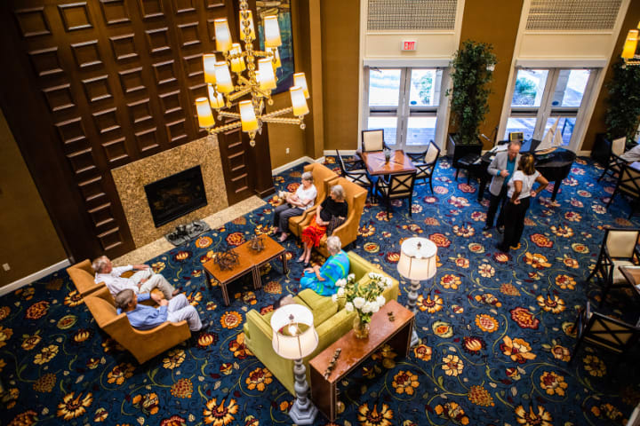 A vibrant hotel lobby with elegant chandeliers, a cozy fireplace, and people relaxing in the seating area.