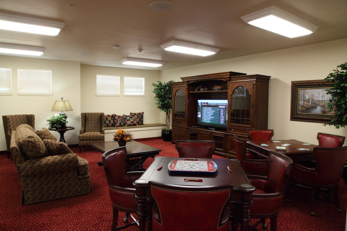 A cozy living room with a television, sofas, chairs, and a table on a red carpeted floor.