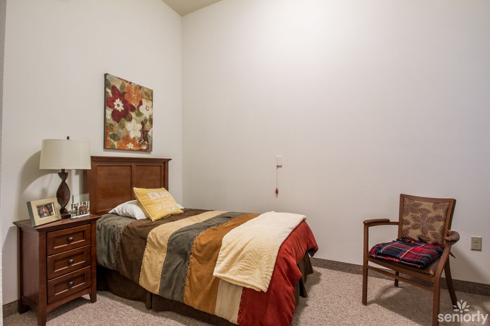 A cozy bedroom with a single bed, decorated with colorful bedding and a floral painting on the wall.