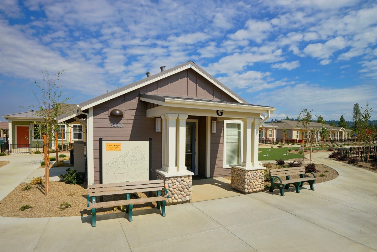 A small house with a porch and benches outside on a sunny day.